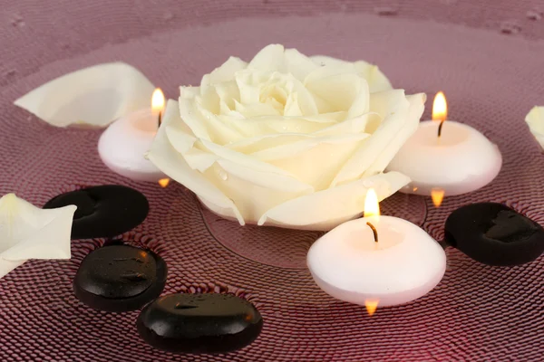 Piedras de spa con flores y velas en agua en el plato —  Fotos de Stock