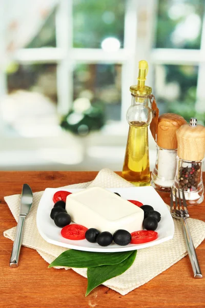Сыр фета на тарелке, украшенный специями и маслом на деревянном столе на фоне окна — стоковое фото
