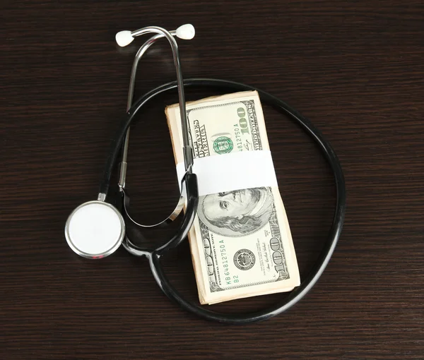 Hälso-och kostnad koncept: stetoskop och dollar på trä bakgrund — Stockfoto