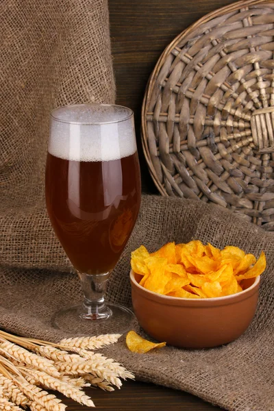 Glass of beer with plate of chips on wooden table on sacking background — Stock Photo, Image