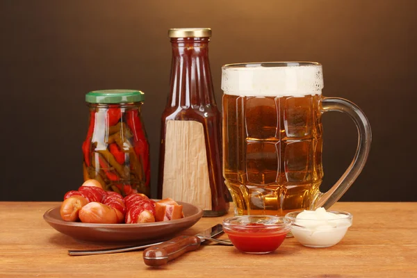 Bier en gegrilde worstjes op houten tafel op bruine achtergrond — Stockfoto