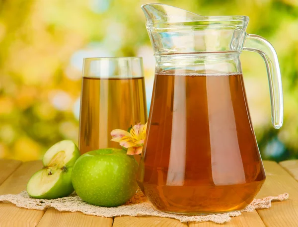 Fullt glas och kanna av äppeljuice och äpplen på träbord utomhus — Stockfoto