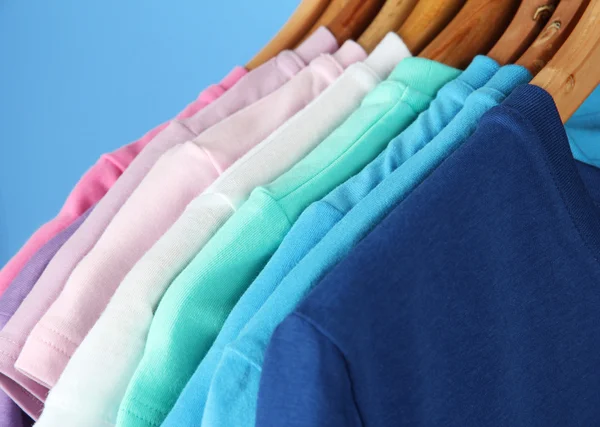 Verscheidenheid van casual shirts op houten hangers, op blauwe achtergrond — Stockfoto