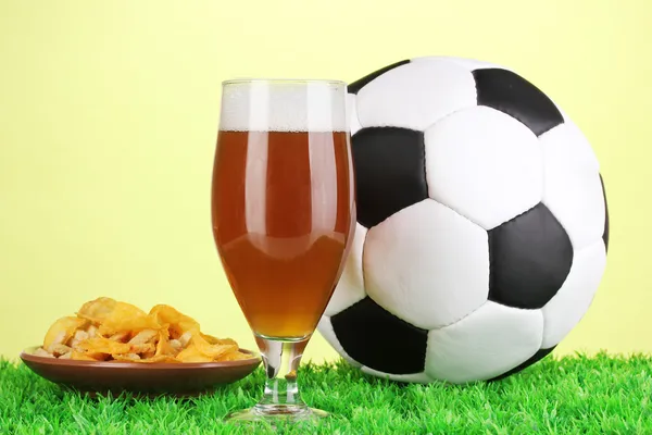 Glass of beer with soccer ball on grass on green background — Stock Photo, Image