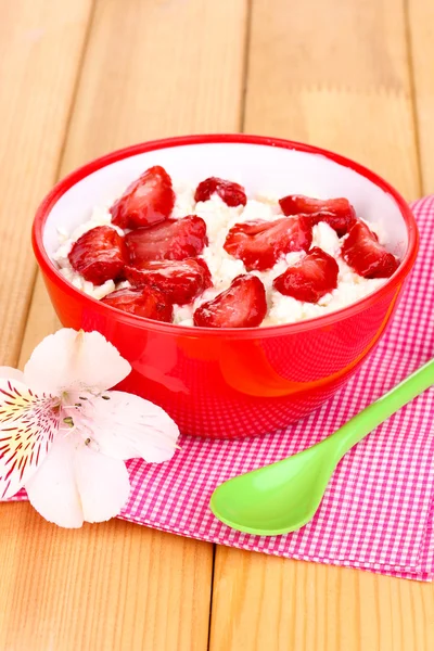 Hüttenkäse in roter Schüssel mit Erdbeeren in Scheiben auf Holztisch — Stockfoto