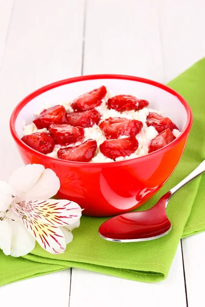 Hüttenkäse in roter Schüssel mit Erdbeerscheiben auf weißem Holztisch — Stockfoto
