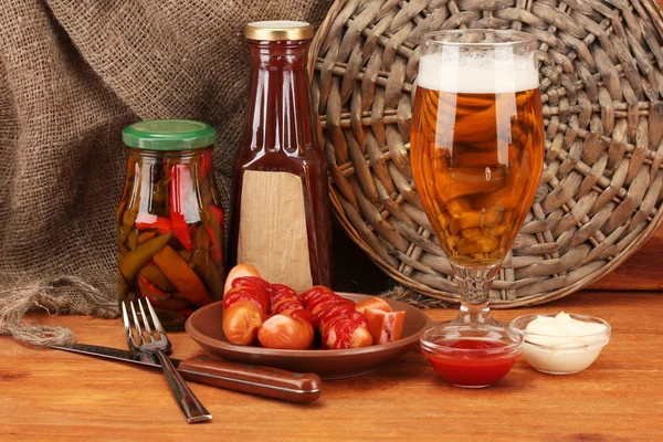 Bière et saucisses grillées sur table en bois sur fond de sac — Photo