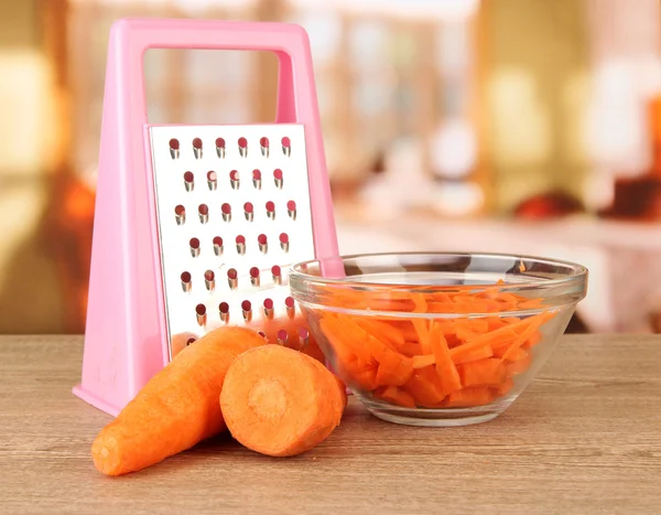 Carrots with grater on table in kitchen — Stock Photo, Image