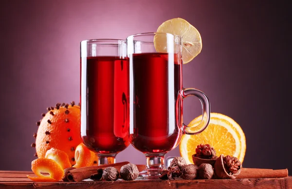 Glühwein in den Gläsern, Gewürz und Orange auf Holztisch auf lila Hintergrund — Stockfoto