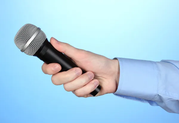 Männliche Hand mit Mikrofon auf blauem Hintergrund — Stockfoto