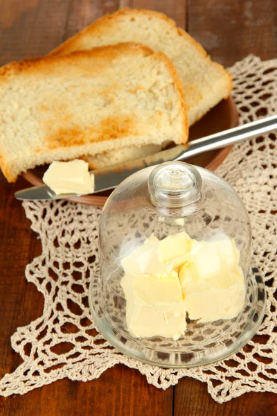 Manteiga em pires de vidro com cobertura de vidro e pão fresco, sobre fundo de madeira — Fotografia de Stock