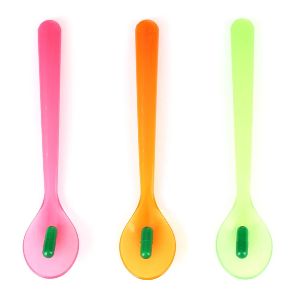 Plastic spoons with color pills, isolated on white — Stock Photo, Image