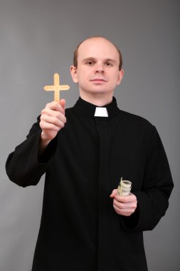 Young pastor with cross and money on gray background