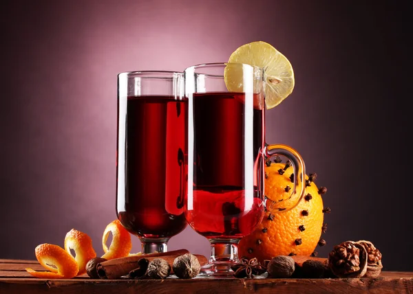 Vin brulè nei bicchieri, spezie e arancia su tavolo di legno su sfondo viola — Foto Stock
