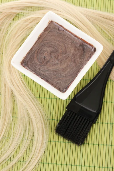 Tintura per capelli in ciotola e pennello per la colorazione dei capelli su tappetino di bambù verde, primo piano — Foto Stock