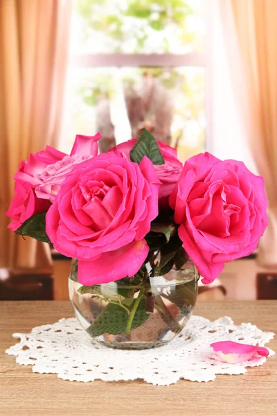 Beautiful pink roses in vase on wooden table on window background — Stock Photo, Image