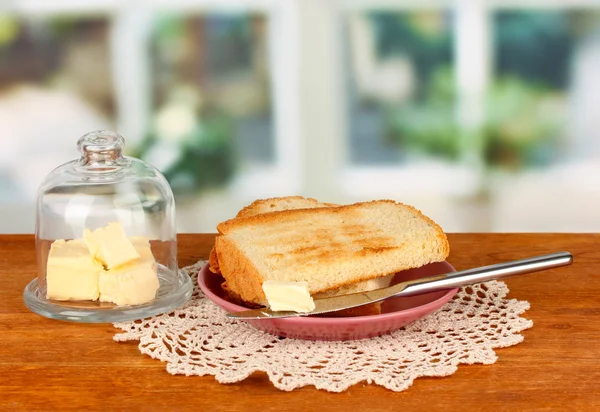 Mantequilla en platillo de vidrio con tapa de vidrio rodeada de pan, sobre fondo brillante — Foto de Stock