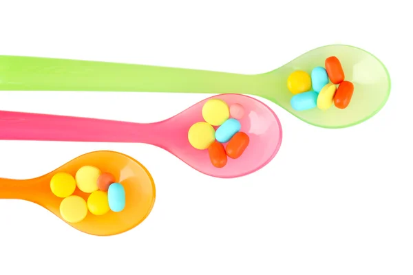 Plastic spoons with color pills, isolated on white — Stock Photo, Image