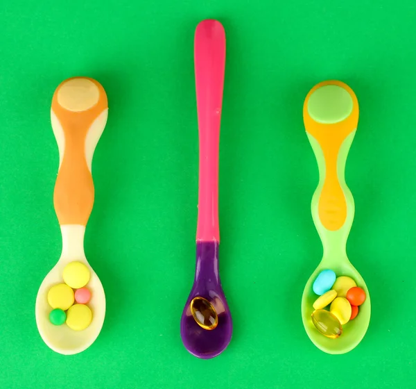 Cucchiai di plastica con pillole di colore, su sfondo verde — Foto Stock
