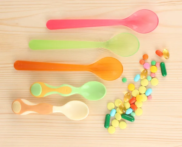 Plastic spoons with color pills on wooden background — Stock Photo, Image