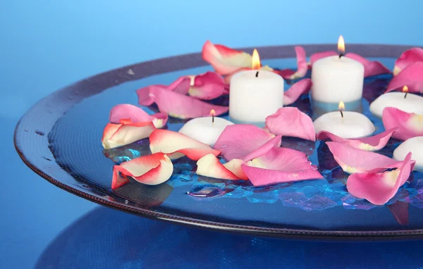 Rosenblätter und Kerzen in Wasser in der Vase auf blauem Hintergrund Nahaufnahme — Stockfoto