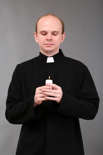 Porträtt av ung pastor anläggning ljus i sin hand, på grå bakgrund — Stockfoto