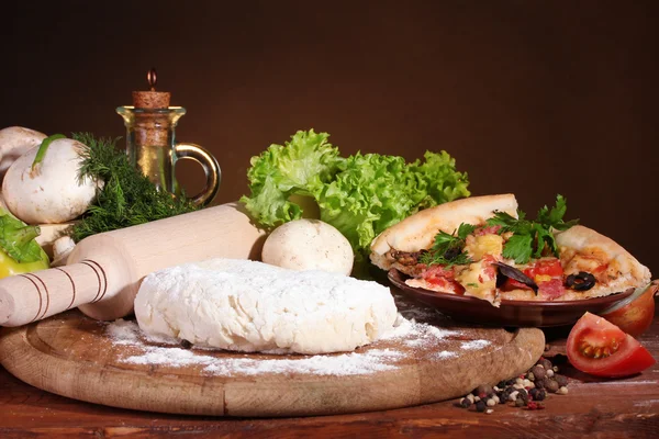 Leckerer Pizzateig, Gewürze und Gemüse auf Holztisch auf braunem Hintergrund — Stockfoto