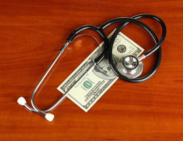 Healthcare cost concept: stethoscope and dollars on wooden background — Stock Photo, Image