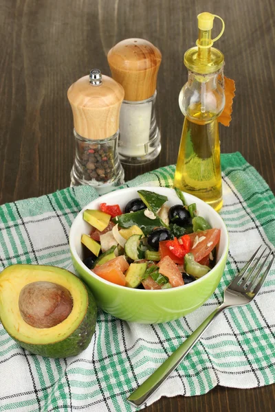 Leckerer Avocadosalat in Schüssel umgeben von Gewürzen auf Holztisch in Großaufnahme — Stockfoto