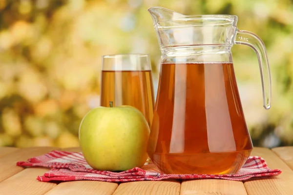 Fullt glas och kanna av äppeljuice och äpple på träbord utomhus — Stockfoto