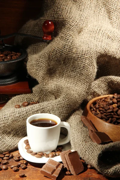 Koffiemolen en kop koffie op bruine houten ondergrond — Stockfoto