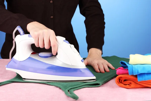 Junge Frau bügelt ihre Kleidung, auf blauem Hintergrund — Stockfoto