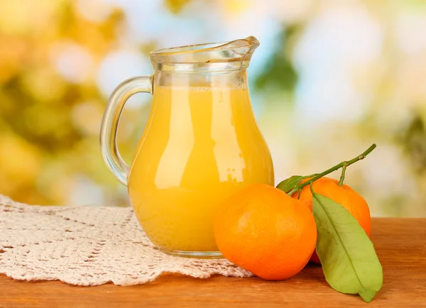 Full jug of orange juice, on wooden table on bright background — Stock Photo, Image