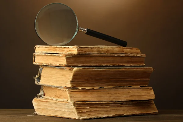 Magnifying glass and books on brown background — Stock Photo, Image