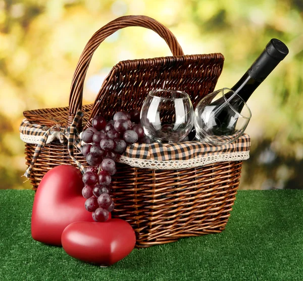 Picnic basket and bottle of wine on grass on bright background — Stock Photo, Image