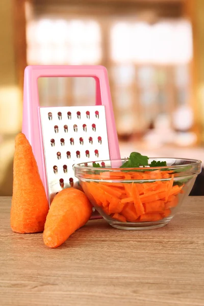 Carrots with grater on table in kitchen — Stock Photo, Image