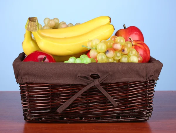 Cesto di vimini con frutta su sfondo colore — Foto Stock