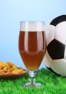 bardak bira ile mavi arka plan üzerinde çim futbol topu