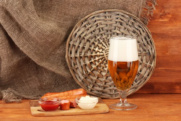 Cerveza y embutidos a la parrilla sobre mesa de madera sobre fondo de saco —  Fotos de Stock