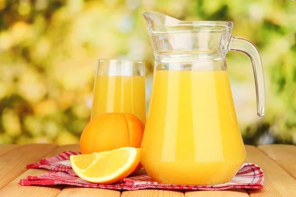 Vol glas en kruik van sinaasappelsap en sinaasappelen op houten tafel buiten — Stockfoto