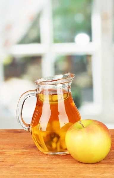 Full kannan av äppeljuice och äpple på träbord på ljus bakgrund — Stockfoto