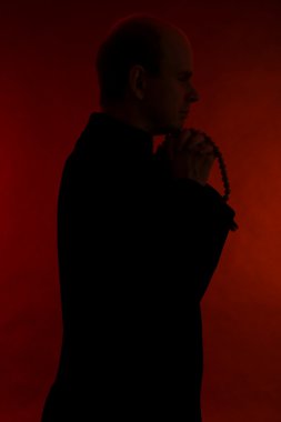 Young pastor with wooden rosary, on dark red background