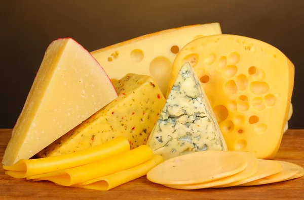 Różne rodzaje sera na drewnianym stole na brązowym tle — Zdjęcie stockowe