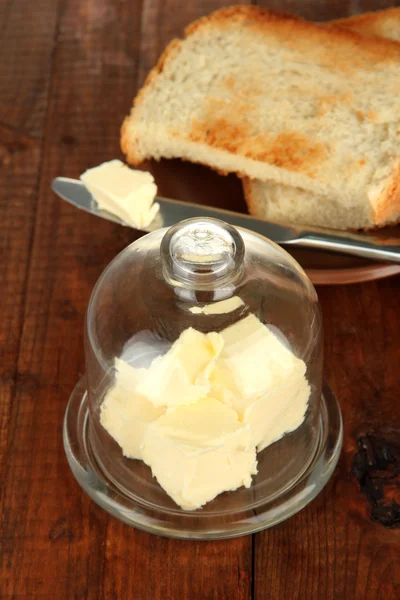 Mantequilla en platillo de vidrio con tapa de vidrio y pan fresco, sobre fondo de madera — Foto de Stock