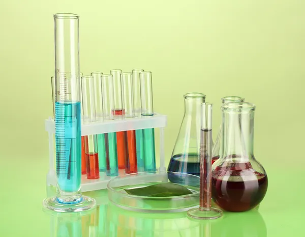 Test-tubes and green leaf tested in petri dish, on color background — Stock Photo, Image