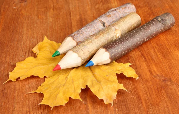 Цветные деревянные карандаши с осенними листьями на деревянном столе — стоковое фото