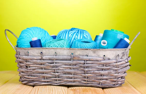 Bright threads in basket on wooden table on green background — Stock Photo, Image