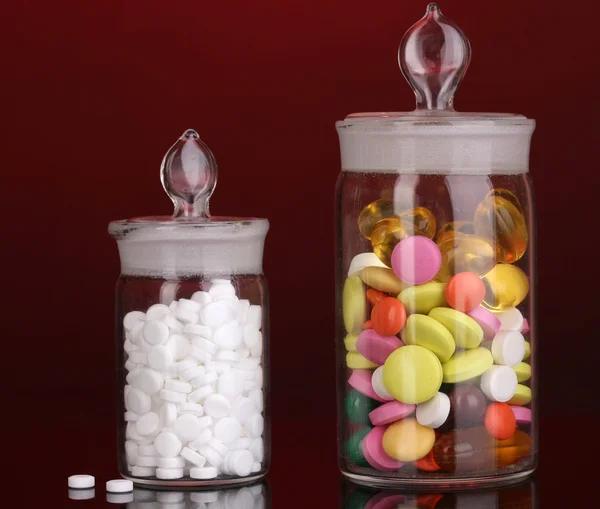 Kapseln und Pillen in Behältern auf rotem Hintergrund — Stockfoto