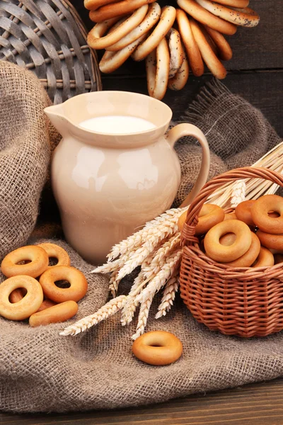 Jar of milk, tasty bagels and spikelets on wooden background — Stock Photo, Image