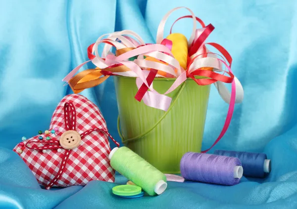 Color bucket with multicolor ribbons and thread on blue fabric background — Stock Photo, Image